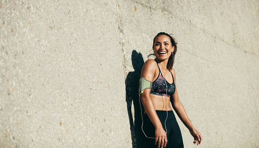 young-woman-in-sports-bra-and-running-tights-leans-against-concrete-wall-while-smiling