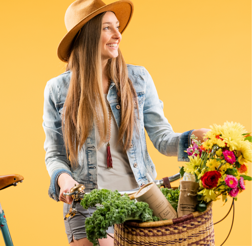Smiling casual woman in straw hat with a wicker basket filled with kale, flowers, and other organic
goods.